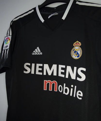 Maillot vintage extérieur noir et blanc du real madrid de la saison 2004-2005. On peut retrouver l'équipementier adidas et le sponsor siemens mobile. Le maillot est floqué du numéro 5 Zinedine Zidane