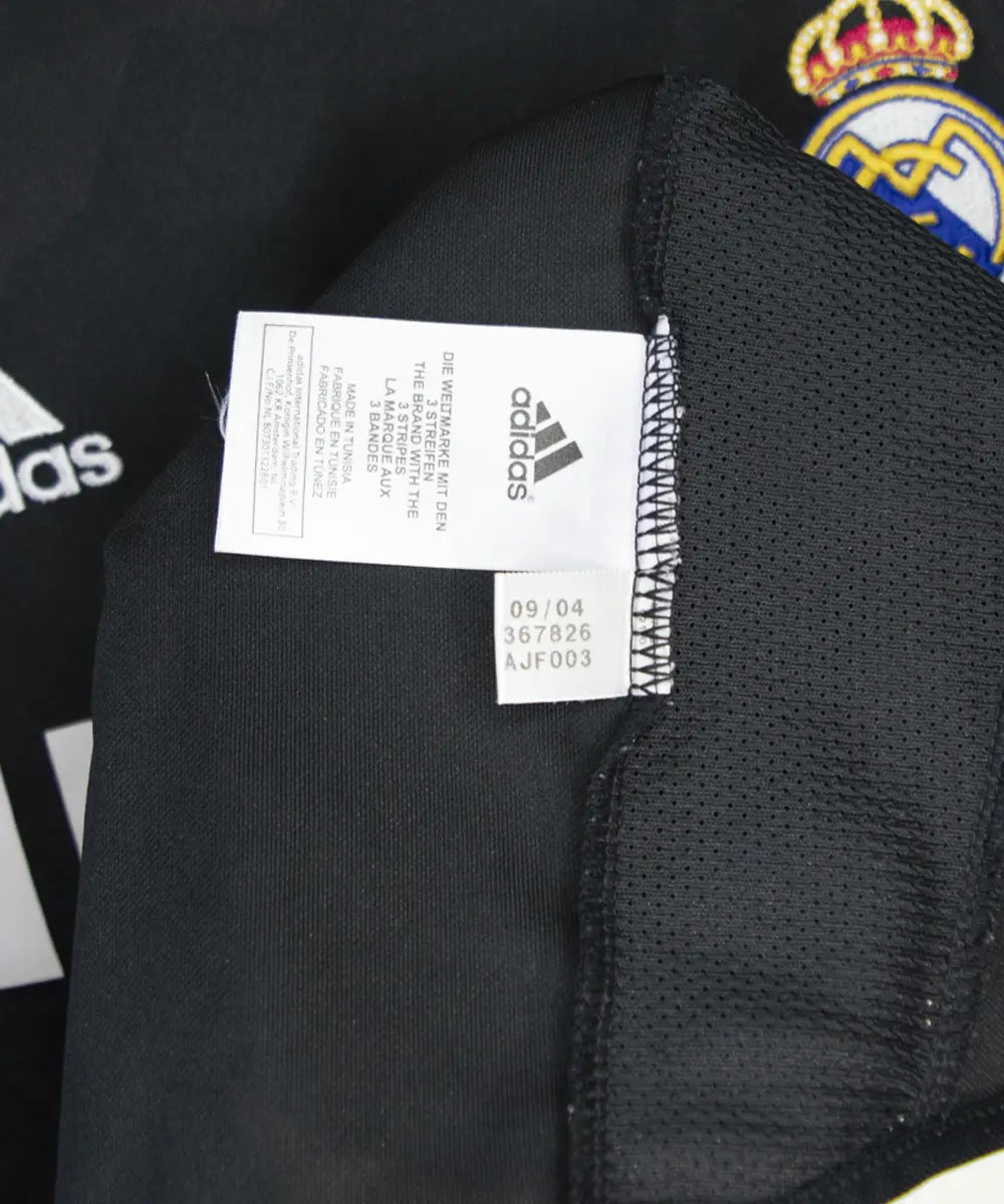 Maillot vintage extérieur noir et blanc du real madrid de la saison 2004-2005. On peut retrouver l'équipementier adidas et le sponsor siemens mobile. Le maillot est floqué du numéro 5 Zinedine Zidane. On peut voir l'étiquette d'authenticité du maillot comportant les numéros 367826