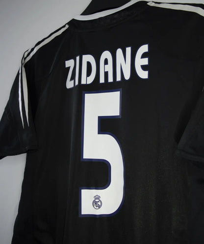 Maillot vintage extérieur noir et blanc du real madrid de la saison 2004-2005. On peut retrouver l'équipementier adidas et le sponsor siemens mobile. Le maillot est floqué du numéro 5 Zinedine Zidane
