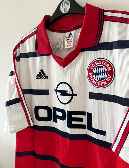 Maillot de foot vintage extérieur blanc et rouge du Bayern Munich 1998/2000. On peut retrouver l'équipementier Adidas et le sponsor Opel. Il s'agit d'un maillot authentique d'époque.