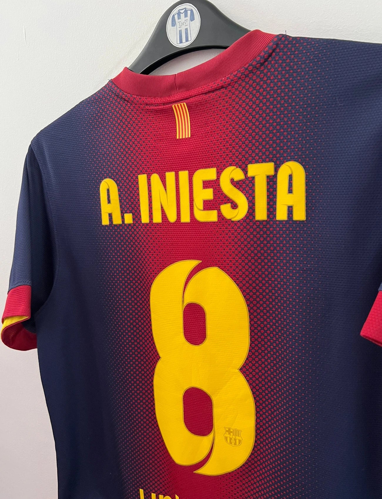 Maillot de foot vintage domicile rouge et bleu du FC Barcelone 2012/2013. On peut retrouver l'équipementier Nike et le sponsor Qatar Foundation. Le maillot est floqué du numéro 8 Andrés Iniesta. Il s'agit d'un maillot authentique d'époque.