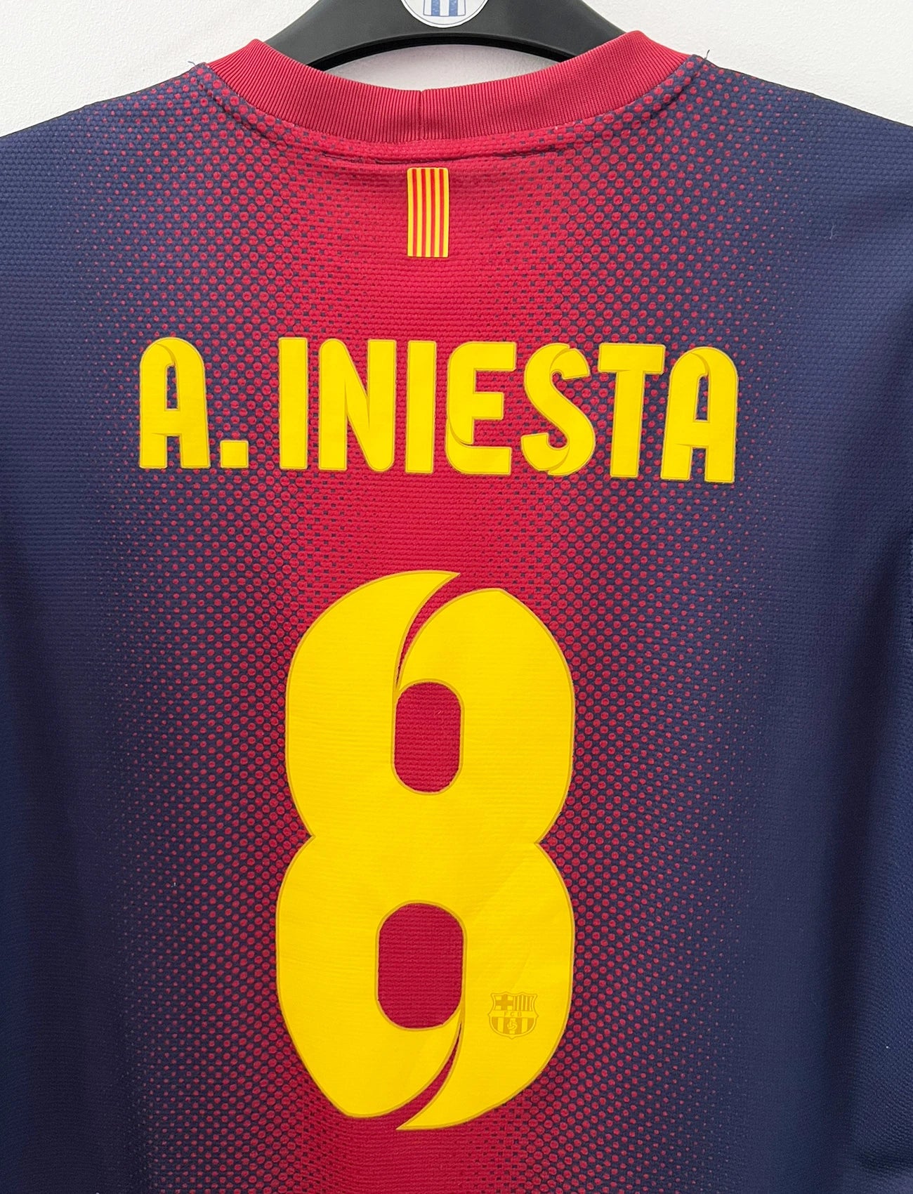 Maillot de foot vintage domicile rouge et bleu du FC Barcelone 2012/2013. On peut retrouver l'équipementier Nike et le sponsor Qatar Foundation. Le maillot est floqué du numéro 8 Andrés Iniesta. Il s'agit d'un maillot authentique d'époque.