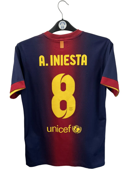 Maillot de foot vintage domicile rouge et bleu du FC Barcelone 2012/2013. On peut retrouver l'équipementier Nike et le sponsor Qatar Foundation. Le maillot est floqué du numéro 8 Andrés Iniesta. Il s'agit d'un maillot authentique d'époque.