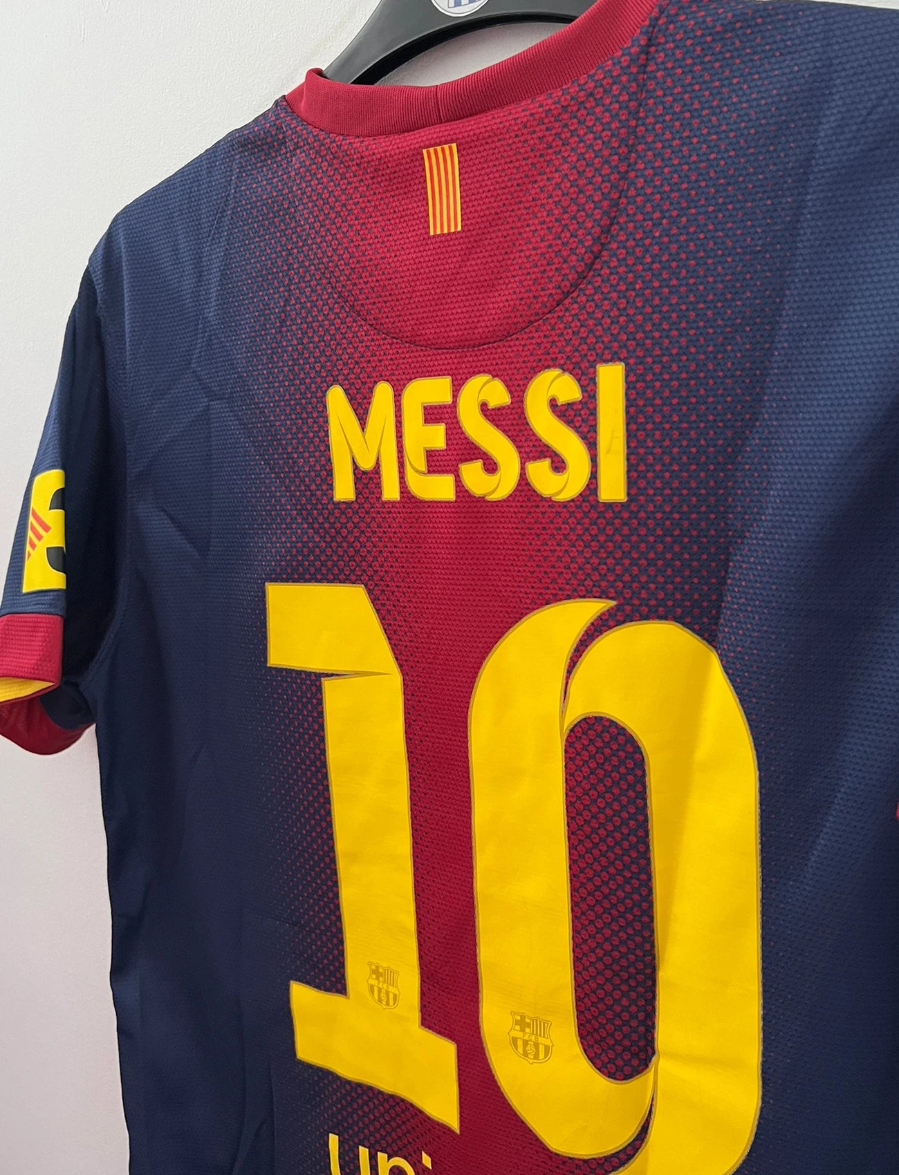 Maillot de foot vintage domicile rouge et bleu du FC Barcelone 2012/2013. On peut retrouver l'équipementier Nike et le sponsor Qatar Foundation. Le maillot est floqué du numéro 10 Lionel Messi. Il s'agit d'un maillot authentique d'époque.