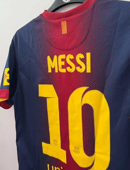 Maillot de foot vintage domicile rouge et bleu du FC Barcelone 2012/2013. On peut retrouver l'équipementier Nike et le sponsor Qatar Foundation. Le maillot est floqué du numéro 10 Lionel Messi. Il s'agit d'un maillot authentique d'époque.