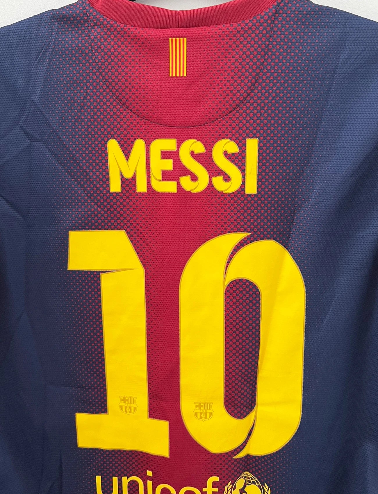 Maillot de foot vintage domicile rouge et bleu du FC Barcelone 2012/2013. On peut retrouver l'équipementier Nike et le sponsor Qatar Foundation. Le maillot est floqué du numéro 10 Lionel Messi. Il s'agit d'un maillot authentique d'époque.