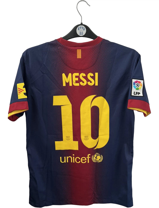 Maillot de foot vintage domicile rouge et bleu du FC Barcelone 2012/2013. On peut retrouver l'équipementier Nike et le sponsor Qatar Foundation. Le maillot est floqué du numéro 10 Lionel Messi. Il s'agit d'un maillot authentique d'époque.