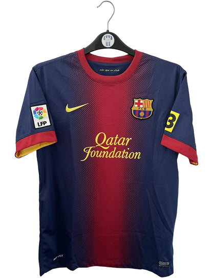 Maillot de foot vintage domicile rouge et bleu du FC Barcelone 2012/2013. On peut retrouver l'équipementier Nike et le sponsor Qatar Foundation. Le maillot est floqué du numéro 10 Lionel Messi. Il s'agit d'un maillot authentique d'époque.