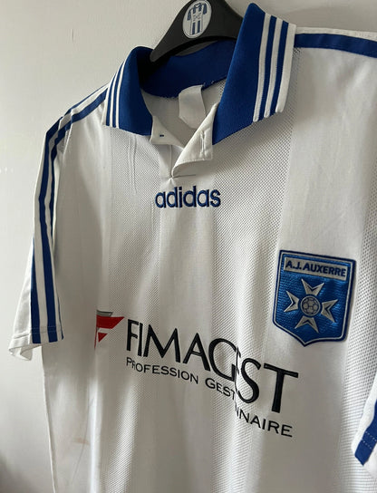 Maillot de foot vintage domicile blanc de l'AJ Auxerre 1997/1998. On peut retrouver l'équipementier Adidas et le sponsor FIMAGEST. Il s'agit d'un maillot authentique d'époque.