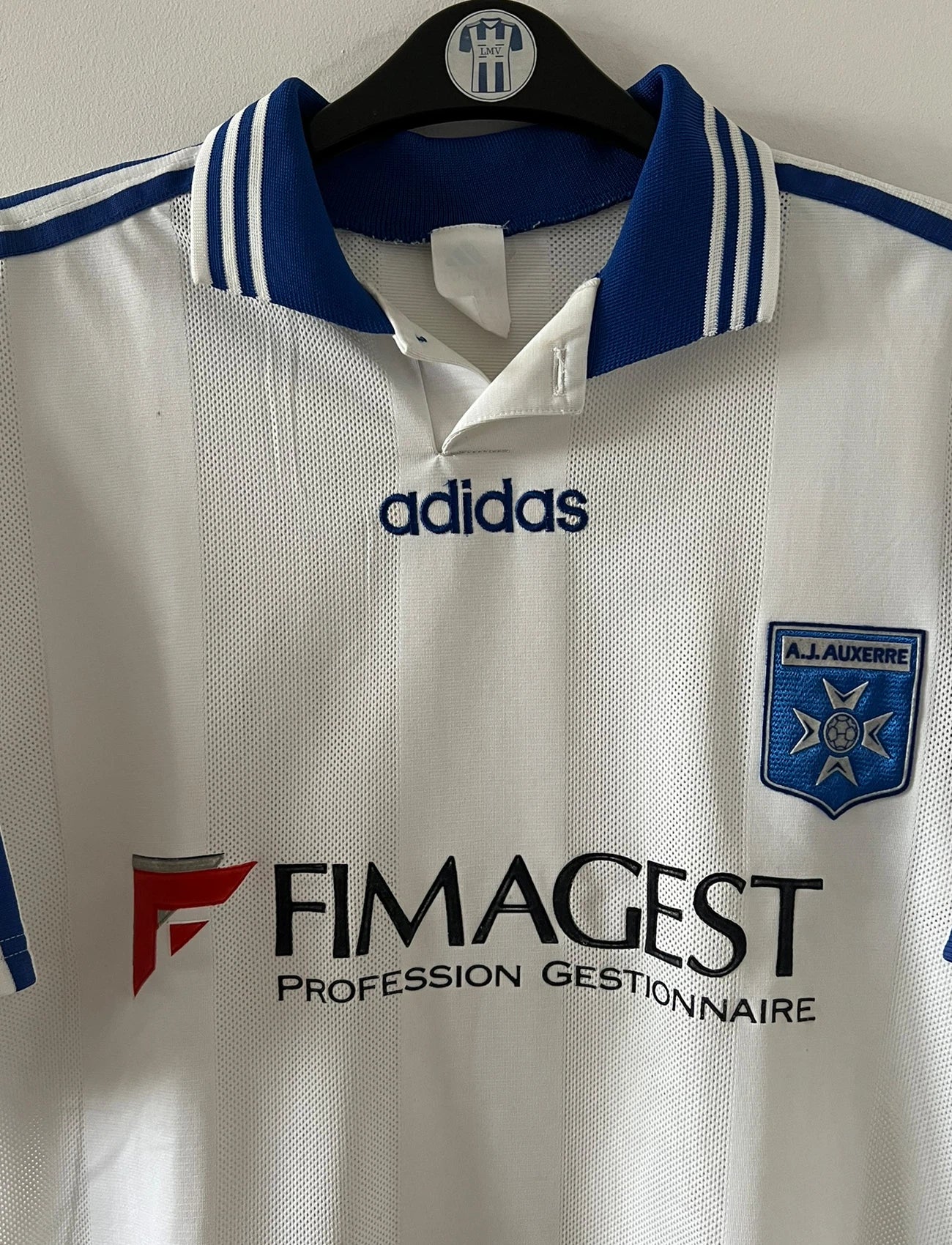 Maillot de foot vintage domicile blanc de l'AJ Auxerre 1997/1998. On peut retrouver l'équipementier Adidas et le sponsor FIMAGEST. Il s'agit d'un maillot authentique d'époque.