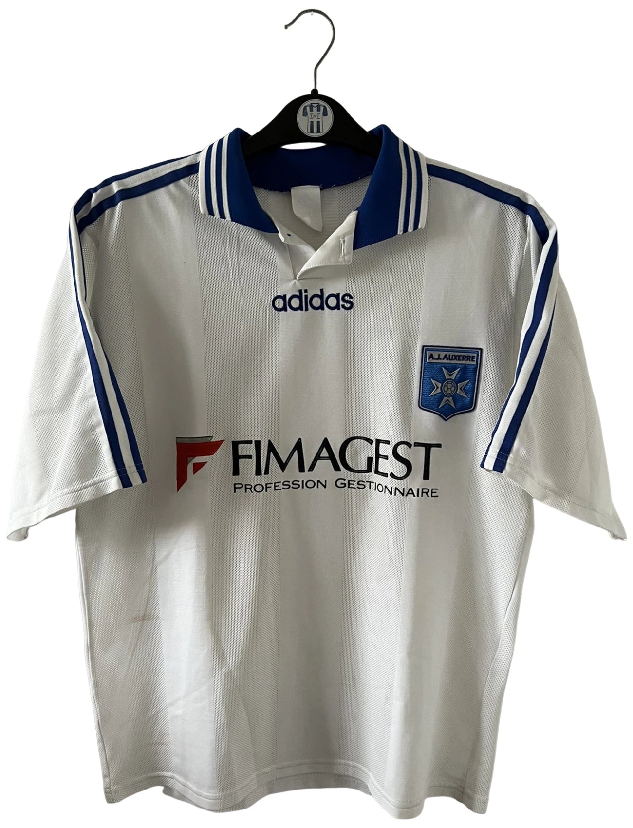 Maillot de foot vintage domicile blanc de l'AJ Auxerre 1997/1998. On peut retrouver l'équipementier Adidas et le sponsor FIMAGEST. Il s'agit d'un maillot authentique d'époque.