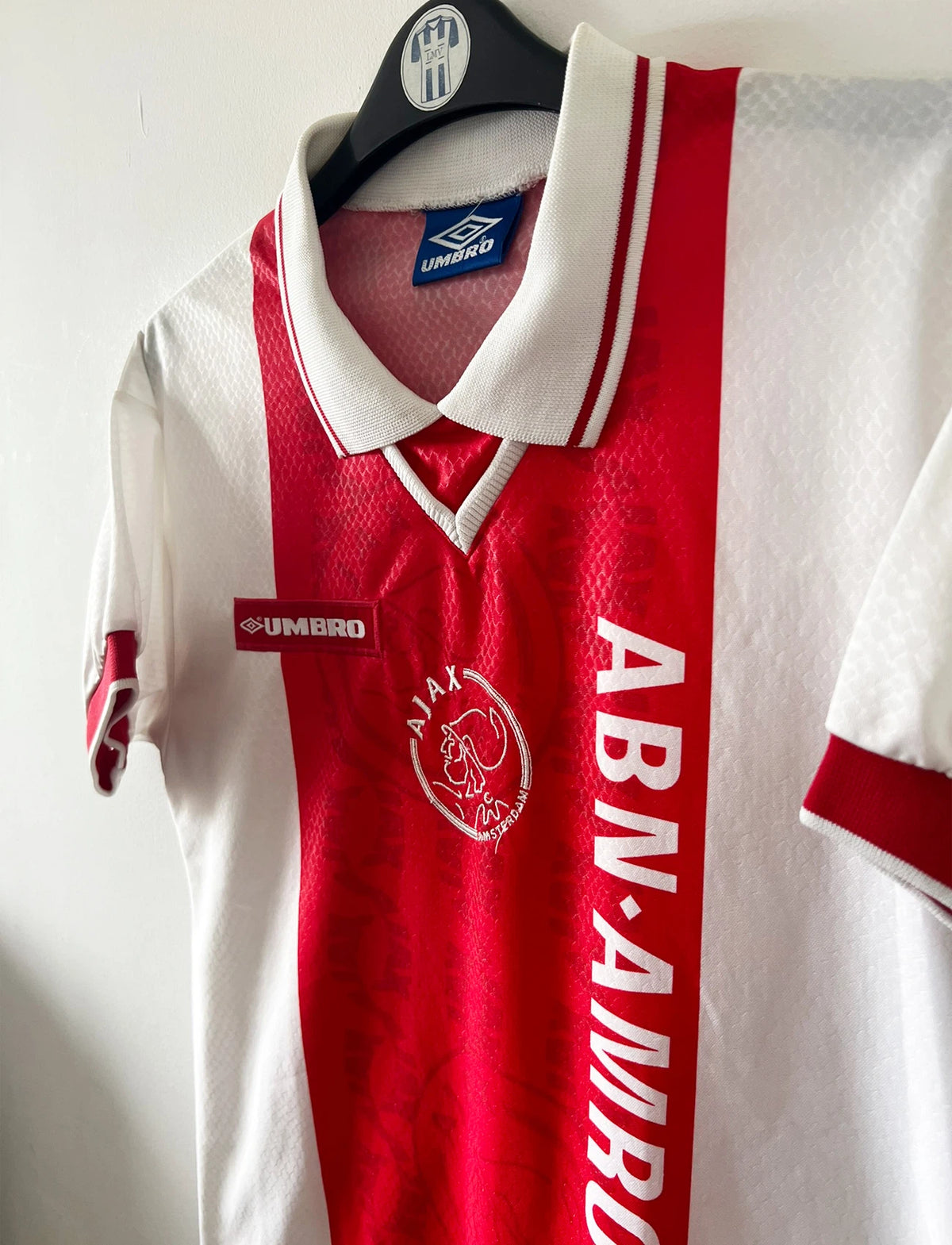 Maillot de foot vintage domicile rouge et blanc de l'Ajax Amsterdam de la saison 1998/1999. On peut retrouver l'équipementier Umbro et le sponsor ABN AMRO. Il s'agit d'un maillot authentique d'époque.