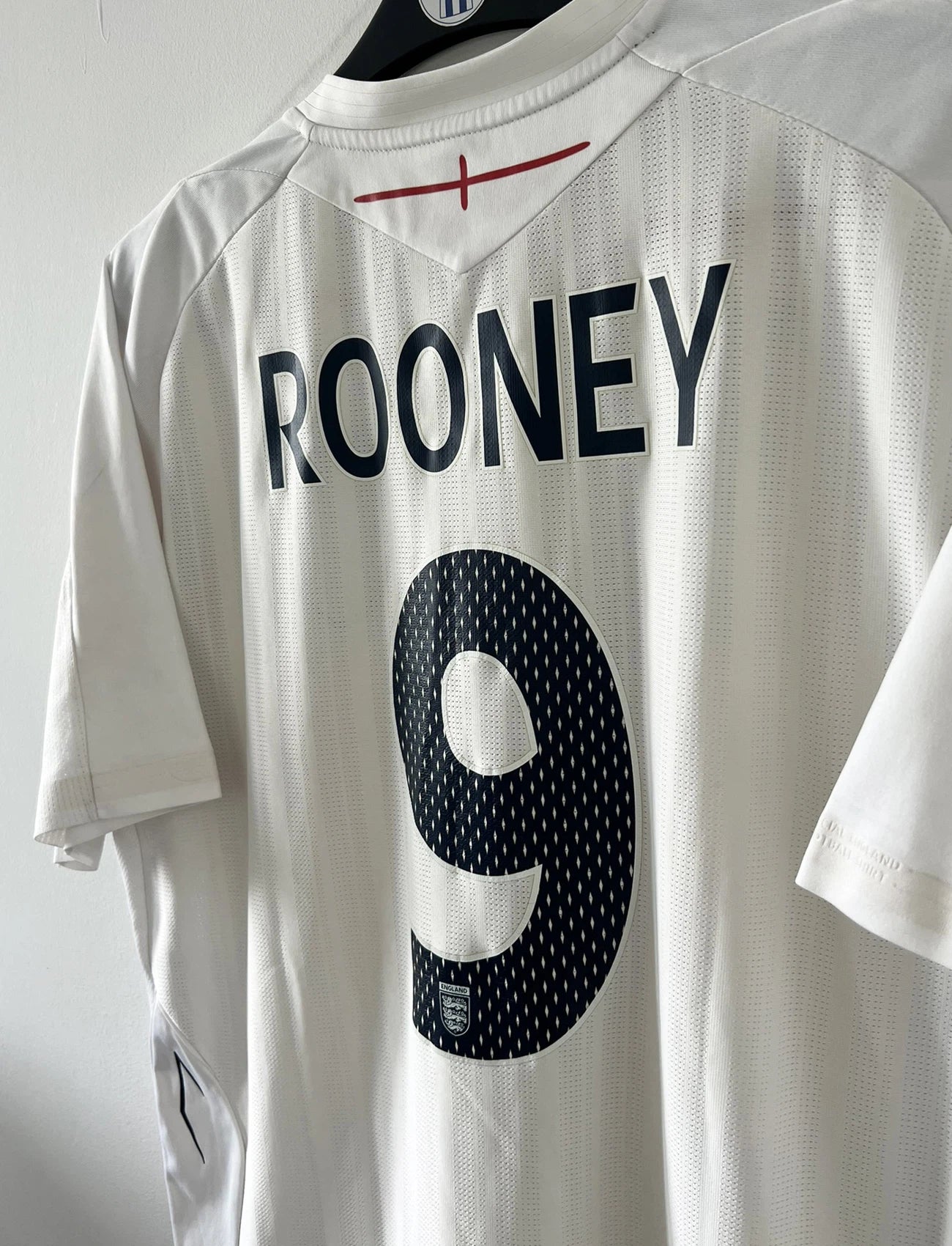 Maillot de foot vintage domicile blanc de l'Angleterre de la saison 2008-2009. On peut y retrouver l'équipementier Umbro. Le maillot est floqué du numéro 9 Rooney. Il s'agit d'un maillot authentique d'époque