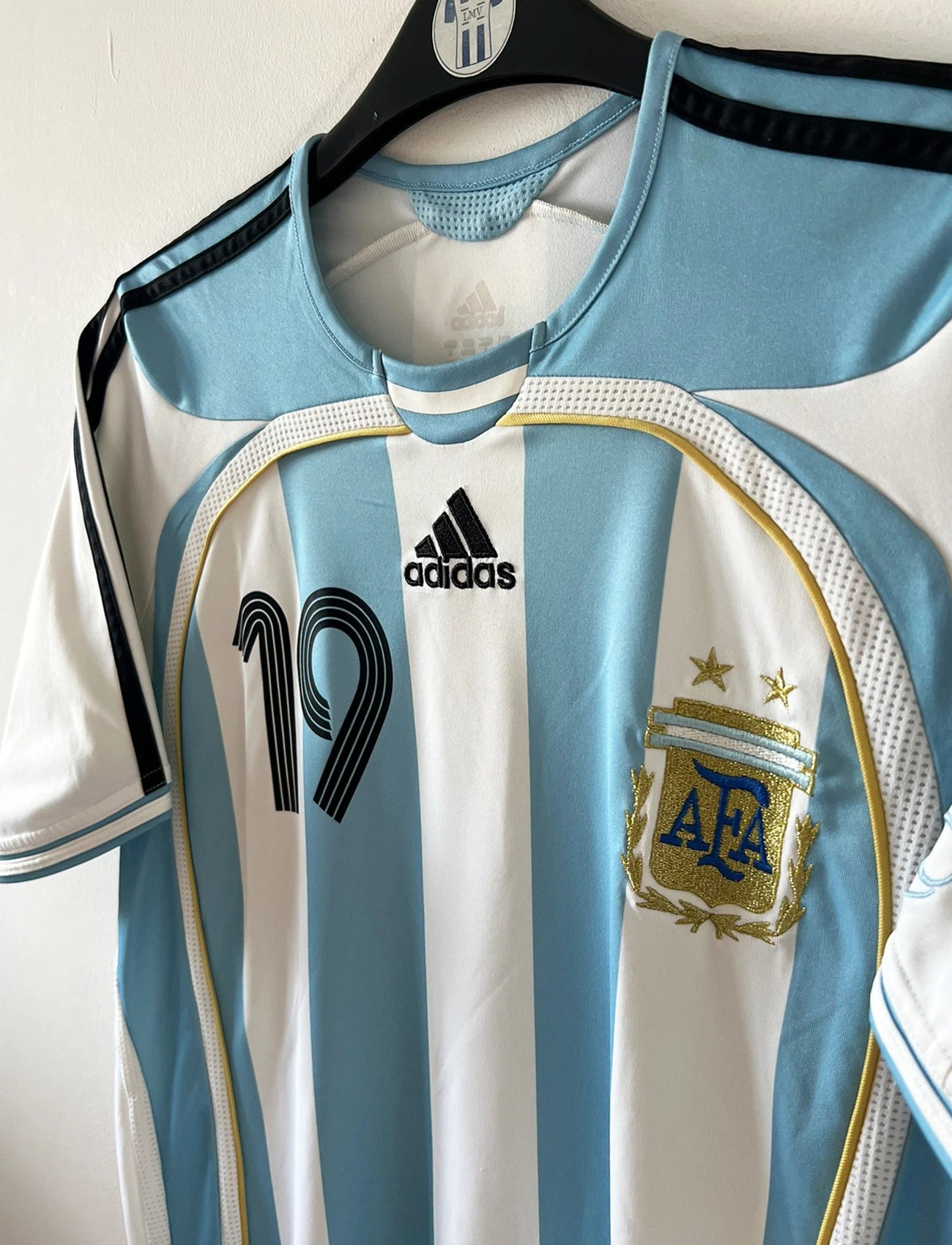 Maillot de foot vintage domicile de l'Argentine 2006. On peut retrouver l'équipementier Adidas. Le maillot est floqué du numéro 19 Messi. Il s'agit d'un maillot authentique d'époque.