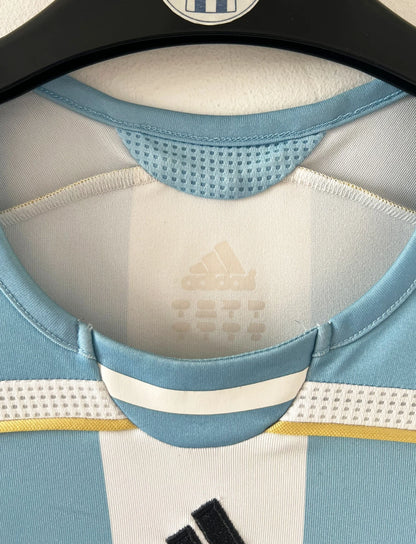 Maillot de foot vintage domicile de l'Argentine 2006. On peut retrouver l'équipementier Adidas. Le maillot est floqué du numéro 19 Messi. Il s'agit d'un maillot authentique d'époque.