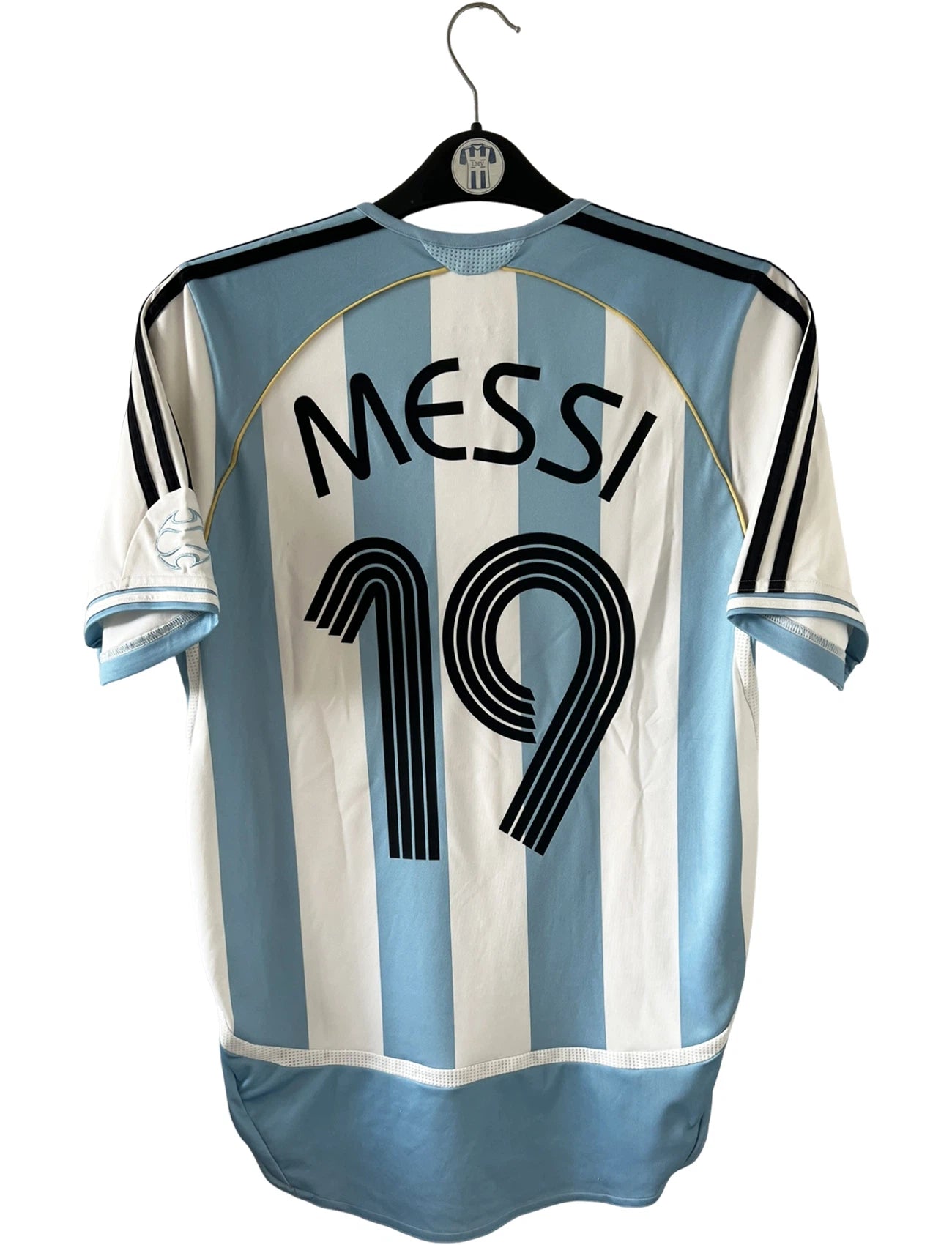 Maillot de foot vintage domicile de l'Argentine 2006. On peut retrouver l'équipementier Adidas. Le maillot est floqué du numéro 19 Messi. Il s'agit d'un maillot authentique d'époque.