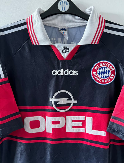 Maillot de foot vintage domicile noir du bayern 1997/1998. On peut retrouver l'équipementier Adidas et le sponsor Opel. Il s'agit d'un maillot authentique d'époque.