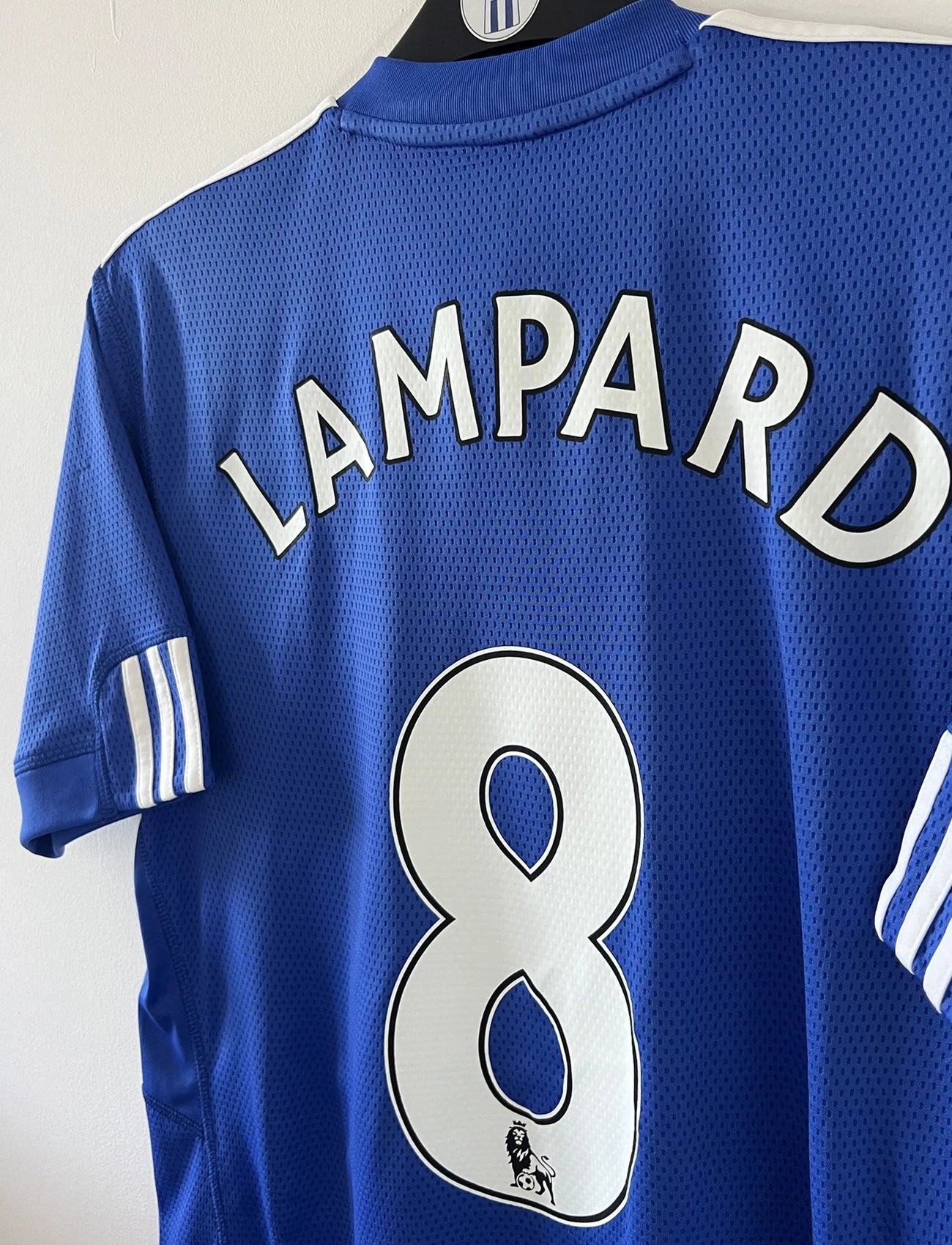 Maillot de foot vinage domicile bleu de chelsea de la saison 2009/2010. On peut retrouver l'équipementier adidas et le sponsor samsung. Le maillot est floqué du numéro 8 Lampard. Il s'agit d'un maillot authentique d'époque comportant les numéros E84291