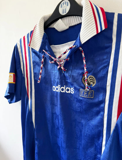 Maillot de foot vintage domicile bleu de l'équipe de france 1996. On peut retrouver l'équipementier Adidas. Il s'agit d'un maillot authentique d'époque.