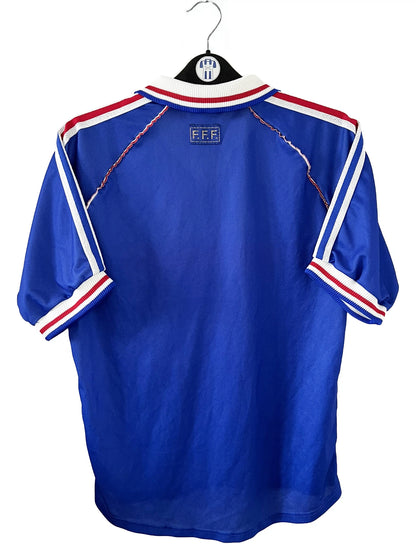 Maillot de foot vintage bleu, blanc et rouge de l'équipe de france 1998. On peut retrouver l'équipementier adidas. Il s'agit d'un maillot authentique édité avant la finale de la coupe du monde car celui-ci ne possède pas l'étoile. Le maillot possède la mention pour toi avec la signature de zidane