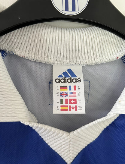 Maillot de foot vintage bleu, blanc et rouge de l'équipe de france 1998. On peut retrouver l'équipementier adidas. Il s'agit d'un maillot authentique édité avant la finale de la coupe du monde car celui-ci ne possède pas l'étoile. Le maillot possède la mention pour toi avec la signature de zidane