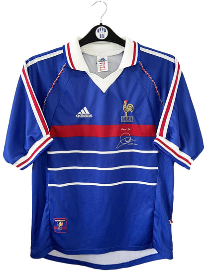 Maillot de foot vintage bleu, blanc et rouge de l'équipe de france 1998. On peut retrouver l'équipementier adidas. Il s'agit d'un maillot authentique édité avant la finale de la coupe du monde car celui-ci ne possède pas l'étoile. Le maillot possède la mention pour toi avec la signature de zidane