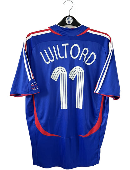 Maillot de foot vintage domicile bleu, blanc et rouge de l'équipe de france 2006. On peut retrouver l'équipementier adidas. Le maillot est floqué du numéro 11 Sylvain Wiltord. Il s'agit d'un maillot authentique d'époque comportant l'étiquette 740126