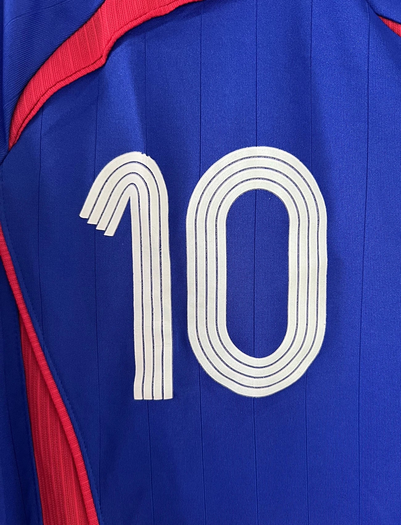 Maillot de foot vintage domicile bleu de l'équipe de france 2006. On peut retrouver l'équipementier adidas. Le maillot est floqué du numéro 10 Zinedine Zidane. Il s'agit d'un maillot authentique comportant l'étiquette 740126.