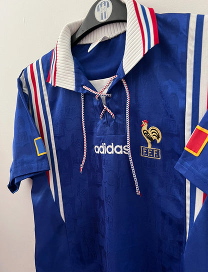 Maillot de foot vintage domicile bleu de l'équipe de france 1996. On peut retrouver l'équipementier Adidas. Il s'agit d'un maillot authentique d'époque.