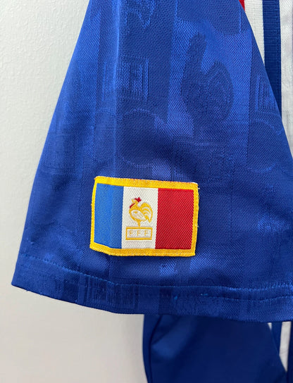 Maillot de foot vintage domicile bleu de l'équipe de france 1996. On peut retrouver l'équipementier Adidas. Il s'agit d'un maillot authentique d'époque.