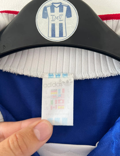 Maillot de foot vintage domicile bleu de l'équipe de france 1996. On peut retrouver l'équipementier Adidas. Il s'agit d'un maillot authentique d'époque.