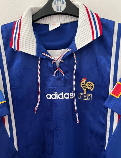 Maillot de foot vintage domicile bleu de l'équipe de france 1996. On peut retrouver l'équipementier Adidas. Il s'agit d'un maillot authentique d'époque.