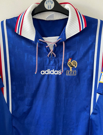 Maillot de foot vintage domicile bleu de l'équipe de france 1996. On peut retrouver l'équipementier Adidas. Il s'agit d'un maillot authentique d'époque.