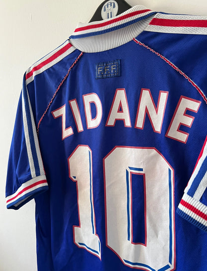 Maillot de foot vintage domicile bleu de l'Equipe de France 1998. On peut retrouver l'équipementier Adidas. Le maillot est floqué du numéro 10 Zinedine Zidane. Il s'agit d'un maillot authentique d'époque.