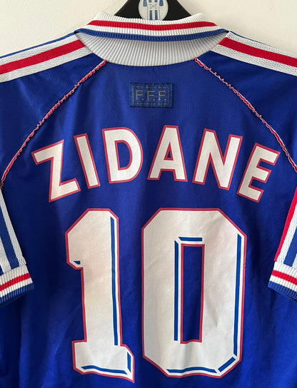 Maillot de foot vintage domicile bleu de l'Equipe de France 1998. On peut retrouver l'équipementier Adidas. Le maillot est floqué du numéro 10 Zinedine Zidane. Il s'agit d'un maillot authentique d'époque.