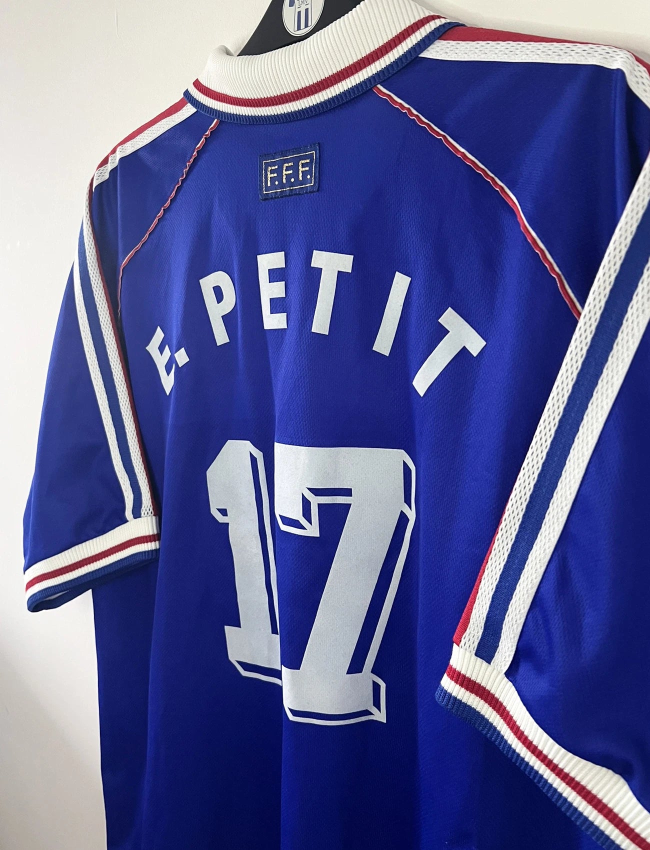 Maillot de foot vintage domicile bleu, blanc et rouge de l'équipe de france 1998. On peut retrouver l'équipementier adidas. Le maillot est floqué du numéro 17 Emmaunel Petit. Il s'agit d'un maillot authentique d'époque