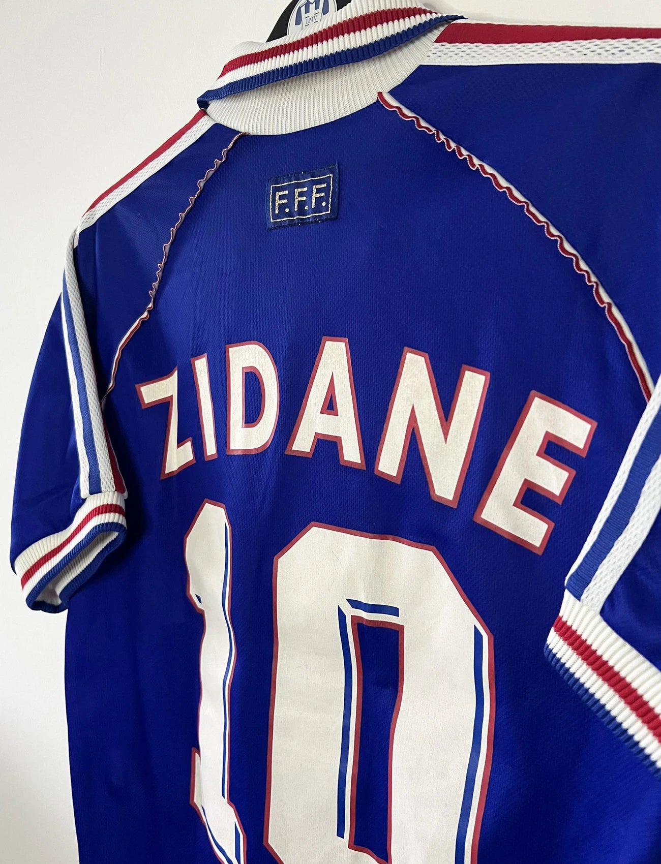 Maillot de foot vintage domicile bleu de l'équipe de france 1998. On peut retrouver l'équipementier Adidas. Le maillot est floqué du numéro 10 Zinedine Zidane. Il s'agit d'un maillot authentique d'époque.