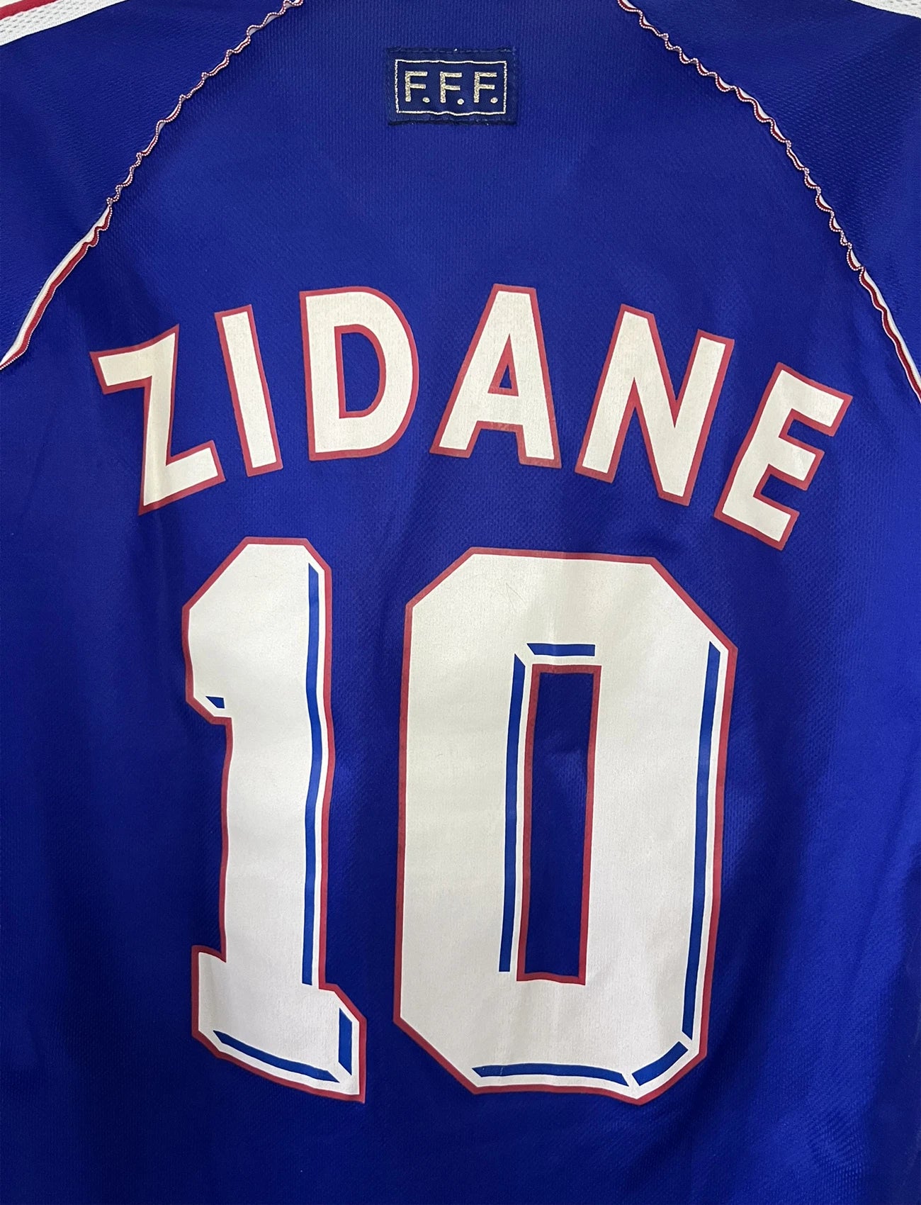 Maillot de foot vintage domicile bleu de l'équipe de france 1998. On peut retrouver l'équipementier Adidas. Le maillot est floqué du numéro 10 Zinedine Zidane. Il s'agit d'un maillot authentique d'époque.