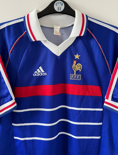 Maillot de foot vintage domicile bleu blanc et rouge de l'équipe de france 1998. On peut retrouver l'équipementier Adidas. Le maillot est floqué du numéro 10 Zinedine Zidane. Il s'agit d'un maillot authentique d'époque.