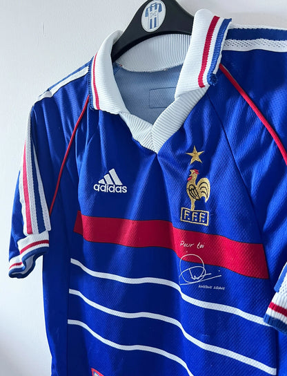 Maillot de foot vintage domicile bleu de l'équipe de France 1998. On peut retrouver l'équipementier Adidas, la signature et le flocage de Zinedine Zidane. Il s'agit d'une magnifique pièce de collection.