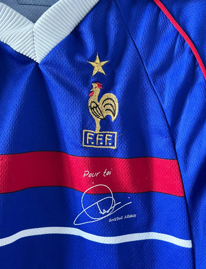 Maillot de foot vintage domicile bleu de l'équipe de France 1998. On peut retrouver l'équipementier Adidas, la signature et le flocage de Zinedine Zidane. Il s'agit d'une magnifique pièce de collection.