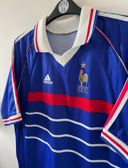 Maillot de foot vintage domicile bleu de l'équipe de france 1998. On peut retrouver l'équipementier Adidas. Le maillot est floqué du numéro 10 Zinedine Zidane. Il s'agit d'un maillot authentique d'époque.