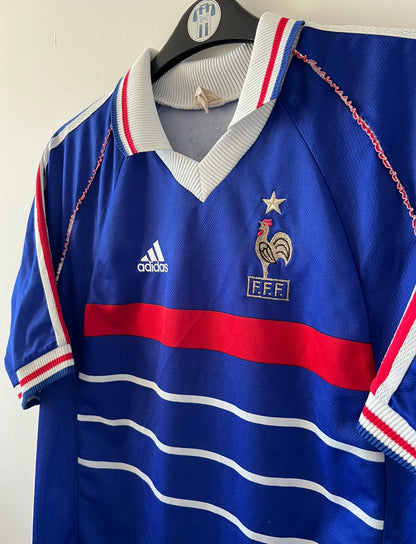 Maillot de foot vintage domicile bleu de l'Equipe de France 1998. On peut retrouver l'équipementier Adidas. Le maillot est floqué du numéro 10 Zinedine Zidane. Il s'agit d'un maillot authentique d'époque.