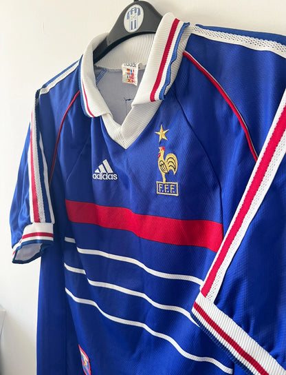 Maillot de foot vintage domicile bleu de l'équipe de france 1998. On peut retrouver l'équipementier Adidas. Le maillot est floqué du numéro 10 Zinedine Zidane. Il s'agit d'un maillot authentique d'époque.