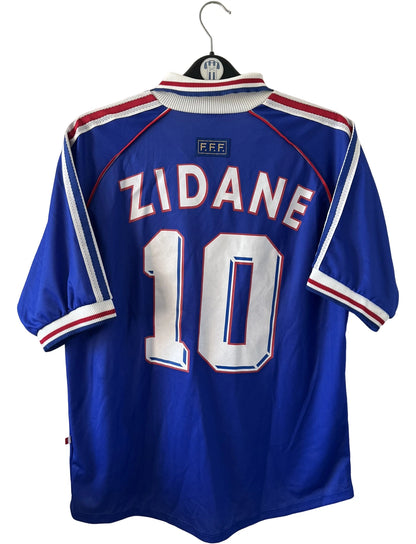 Maillot de foot vintage domicile bleu de l'équipe de france 1998. On peut retrouver l'équipementier Adidas. Le maillot est floqué du numéro 10 Zinedine Zidane. Il s'agit d'un maillot authentique d'époque.