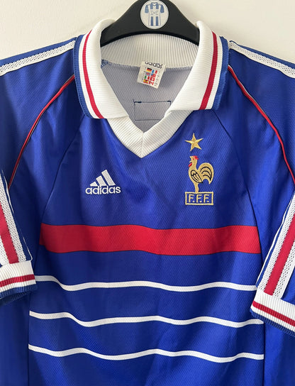 Maillot de foot vintage domicile bleu de l'équipe de france 1998. On peut retrouver l'équipementier Adidas. Le maillot est floqué du numéro 10 Zinedine Zidane. Il s'agit d'un maillot authentique d'époque.