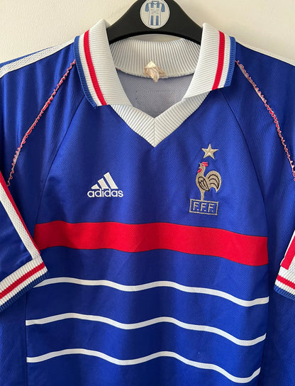 Maillot de foot vintage domicile bleu de l'Equipe de France 1998. On peut retrouver l'équipementier Adidas. Le maillot est floqué du numéro 10 Zinedine Zidane. Il s'agit d'un maillot authentique d'époque.