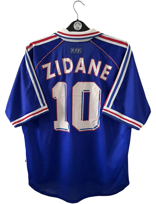 Maillot de foot vintage domicile bleu de l'équipe de france 1998. On peut retrouver l'équipementier Adidas. Le maillot est floqué du numéro 10 Zinedine Zidane. Il s'agit d'un maillot authentique d'époque.