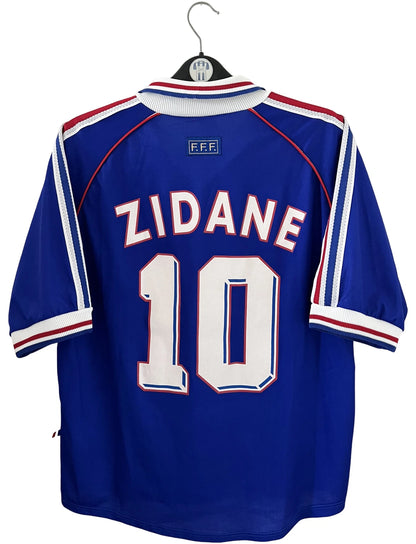 Maillot foot vintage domicile equipe de france 1998 bleu blanc et rouge. On peut retrouver l'équipementier adidas. Le maillot est floqué du numéro 10 Zinedine Zidane. Il s'agit d'un maillot authentique d'époque vendu avec son short d'époque.