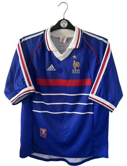 Maillot de foot vintage domicile bleu de l'équipe de france 1998. On peut retrouver l'équipementier Adidas. Le maillot est floqué du numéro 10 Zinedine Zidane. Il s'agit d'un maillot authentique d'époque.